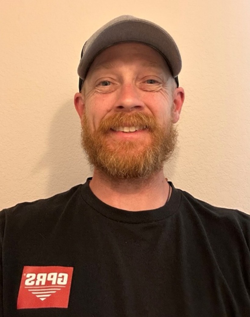 A GPRS Project Manager with a red beard wearing a black t-shirt with the GPRS logo on the left side of the shirt, along with a baseball hat. 