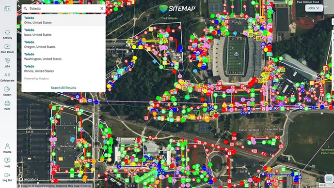 Screenshot of SiteMap displaying an aerial view of a campus or large facility. The map is densely populated with color-coded symbols, lines, and markers representing underground and above-ground assets. A search panel on the left shows results for “Toledo” in multiple U.S. states, while navigation and collaboration tools appear in a vertical menu. The interface includes the “SITEMAP” logo and overlays detailed utility network data on top of satellite imagery featuring roads, buildings, parking lots, and a sports stadium.