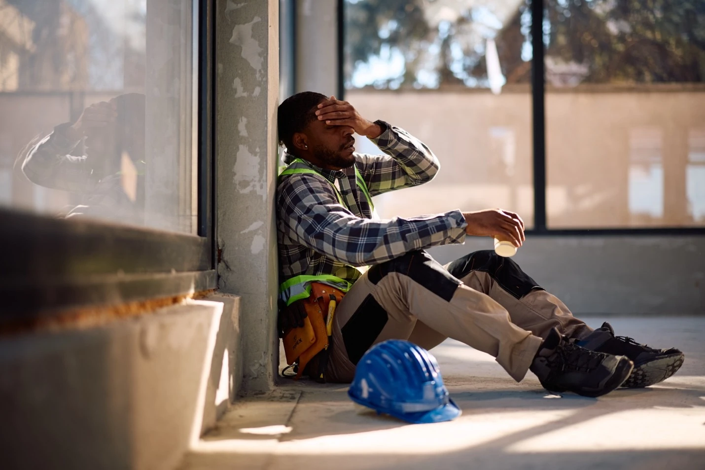 A construction worker sits and rests against a concrete wall, illustrating the fatigue and heat exhaustion symptoms AEC teams need to recognize during summer months.