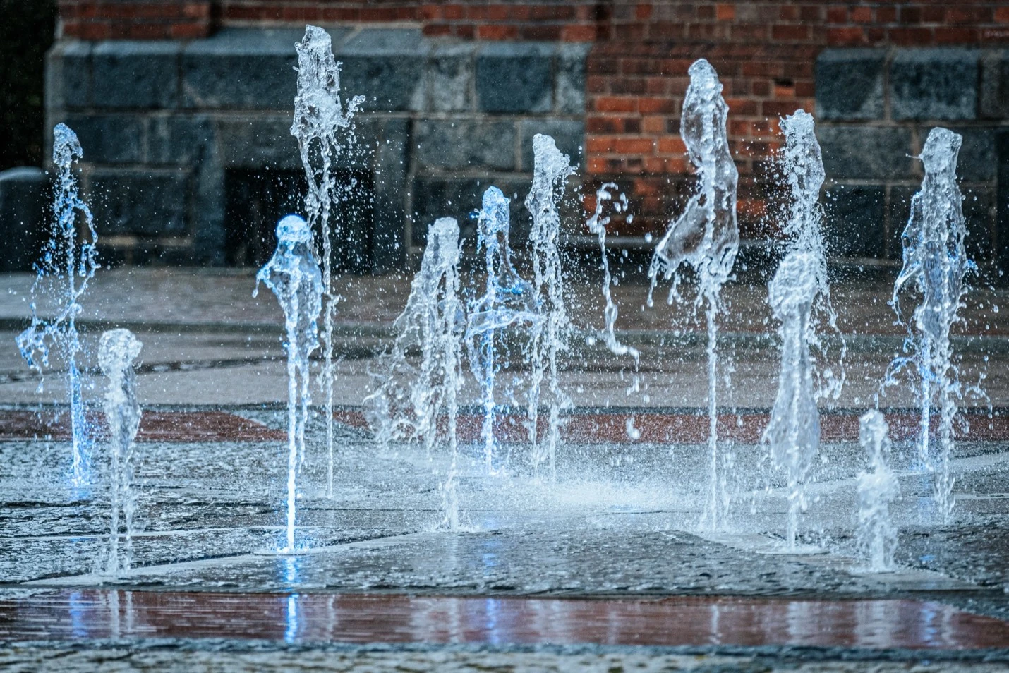 Cool water jets rise in an outdoor plaza, a visual cue for the hydration breaks and cooling stations that protect AEC crews from heat-related illness.