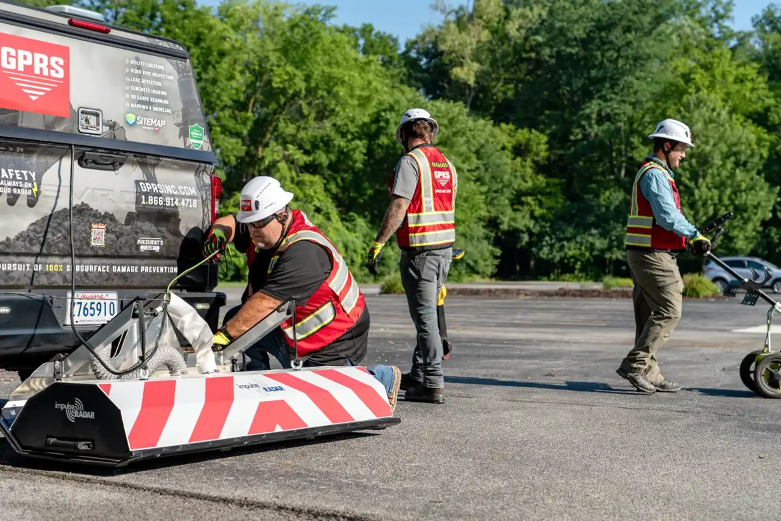 A GPRS Project Manager pushes a GPR cart across open ground on a job site, while two other Project Managers stage equipment for work that demands heat safety protocols when temperatures climb.