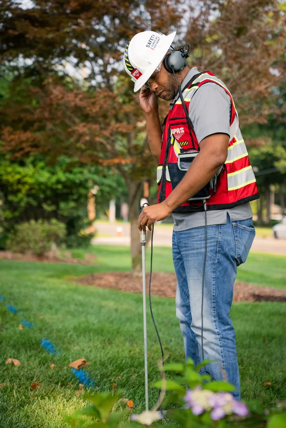  A project manager in a safety vest and headphones stands in grass, focused on GPRS leak detection work.