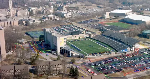 A stadium with a blue field and a large parking lot. | GPRS Images