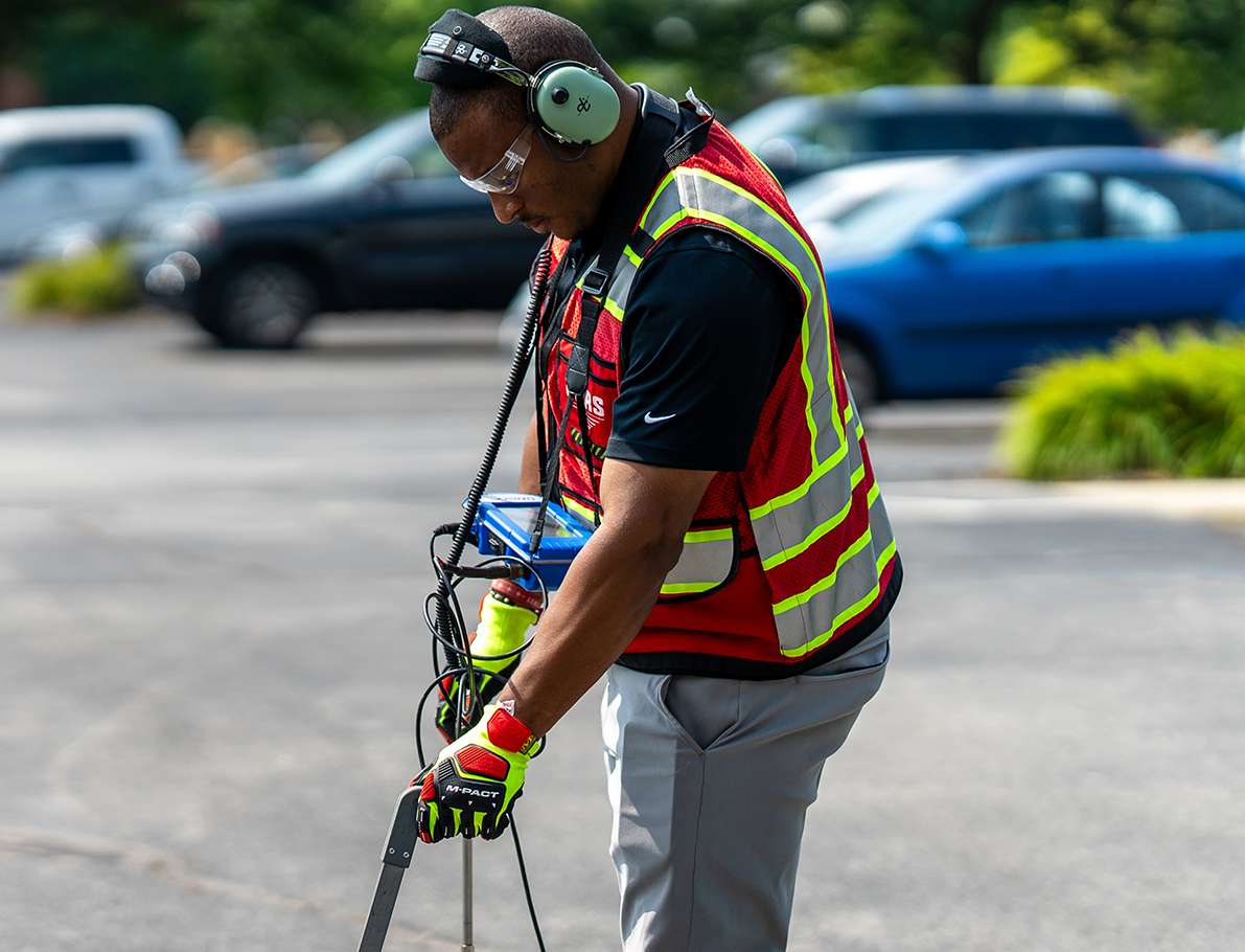 A GPRS project manager in a safety vest conducts leak detection using a specialized tool.