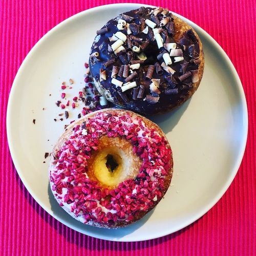 Two donuts with brown and pink sprinkles on a pink background