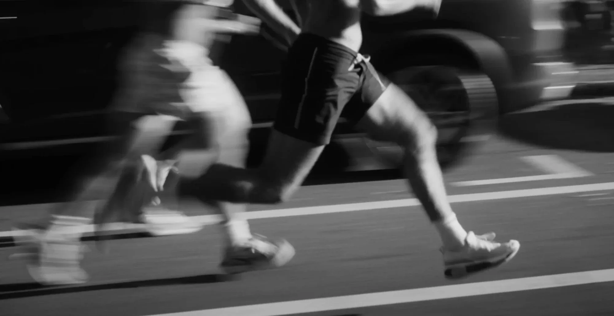 Black-and-white motion blur of runners' legs on a road at night.