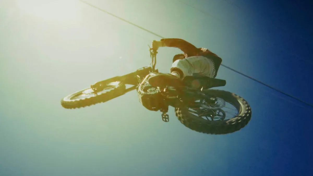 A dirt-bike rider silhouetted mid-air against a teal-to-blue sky.