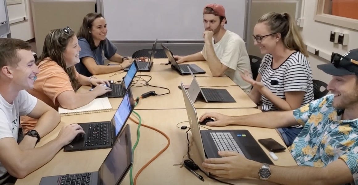 Students sitting with computers around a large table