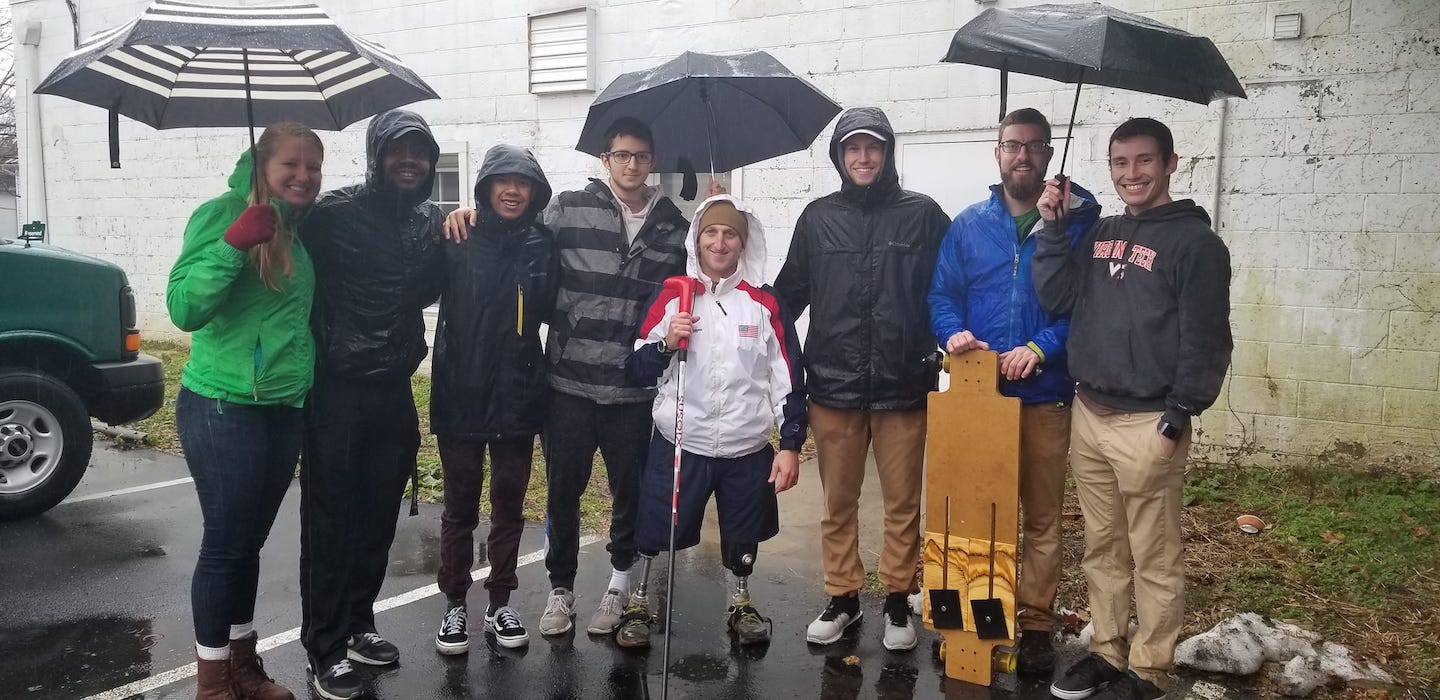 A group of students stand with a Challenger under umbrellas