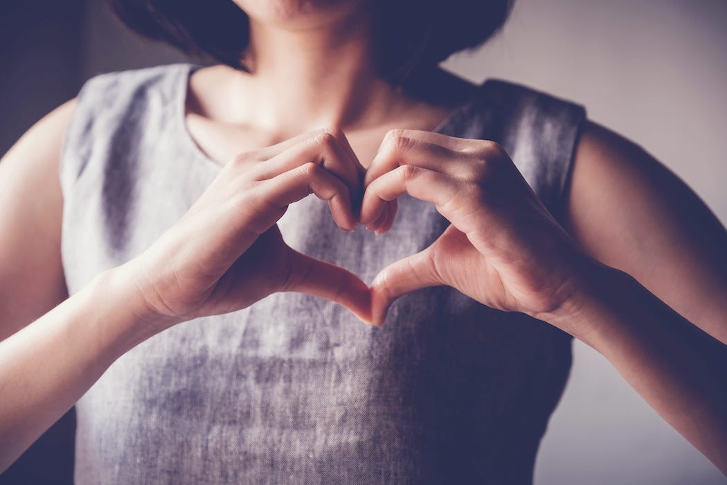 A woman making a heart with her hands in front of herself.