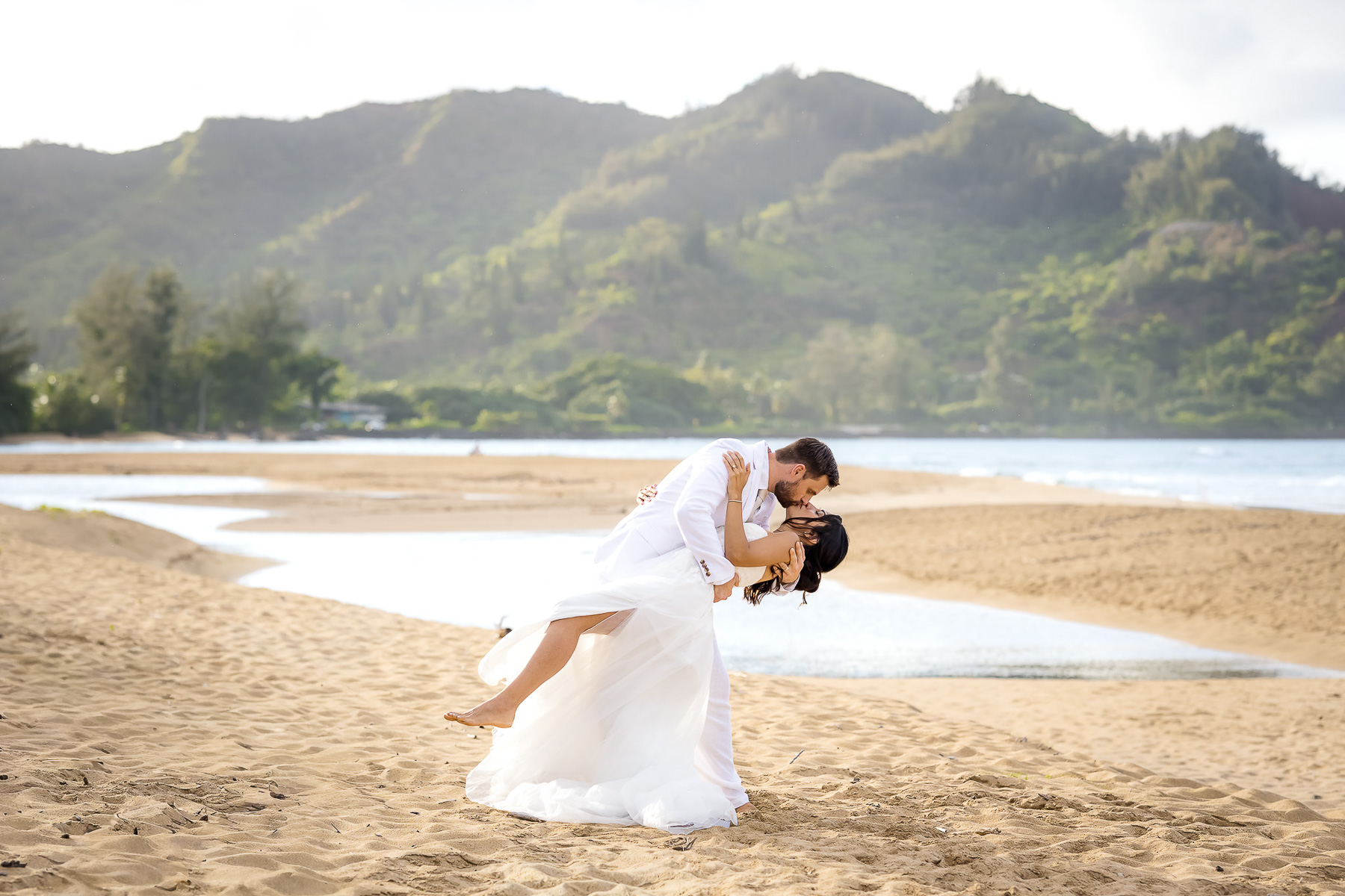 Groom dipping the bride on the beach at sunset, documented by a Kauai elopement photographer.