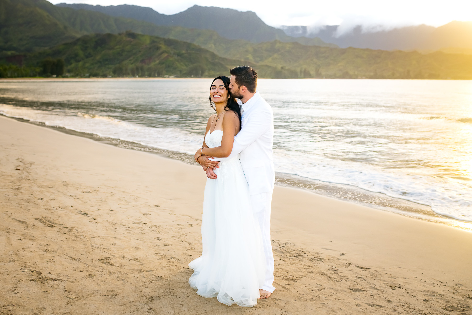 Groom embracing his bride on the beach.h