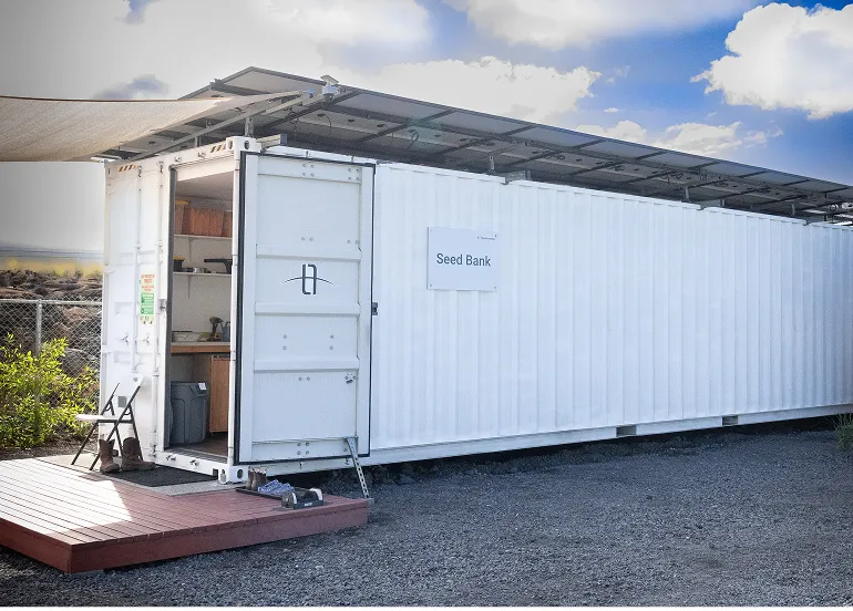 White Seed Bank container with open door and solar panels on roof outdoors under blue sky.
