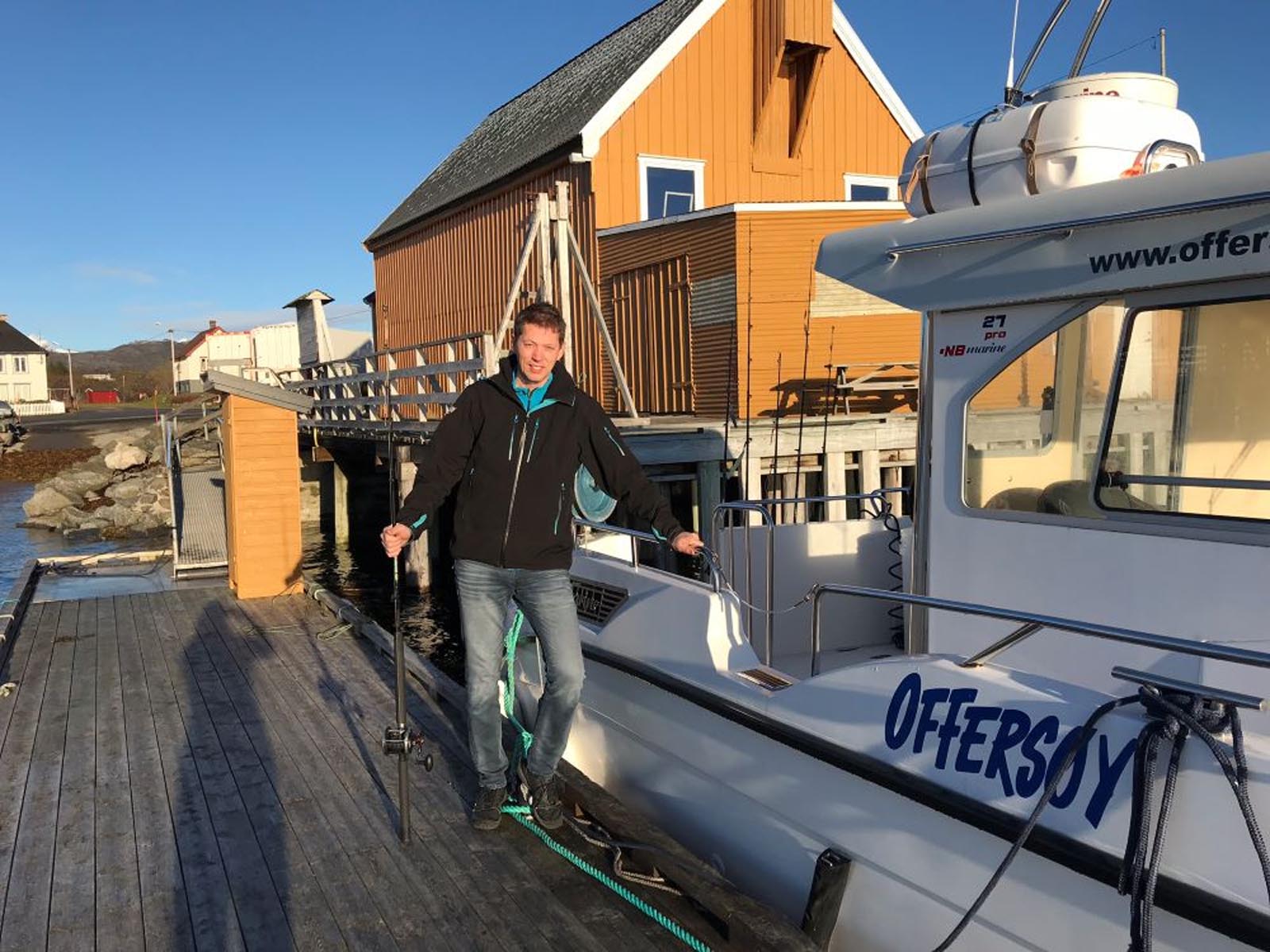 Mann med fiskestang ved fiskebåt til leie ved brygga på Offersøy