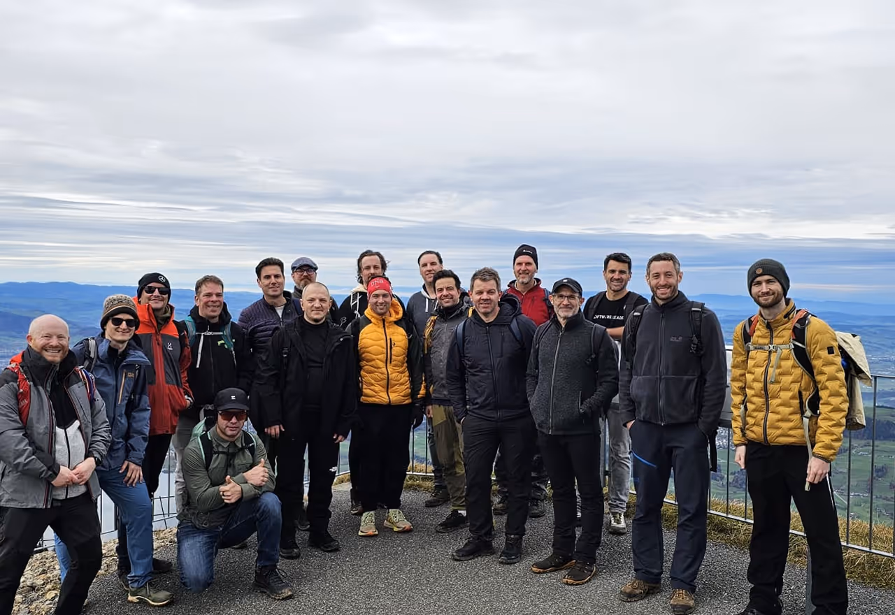 Group of men dressed in outdoor gear posing on a mountain overlook under cloudy sky.