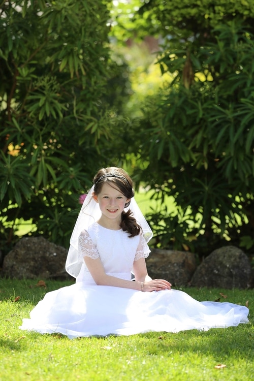 Communion girl sitting on the grass by Jenny Callanan Photography