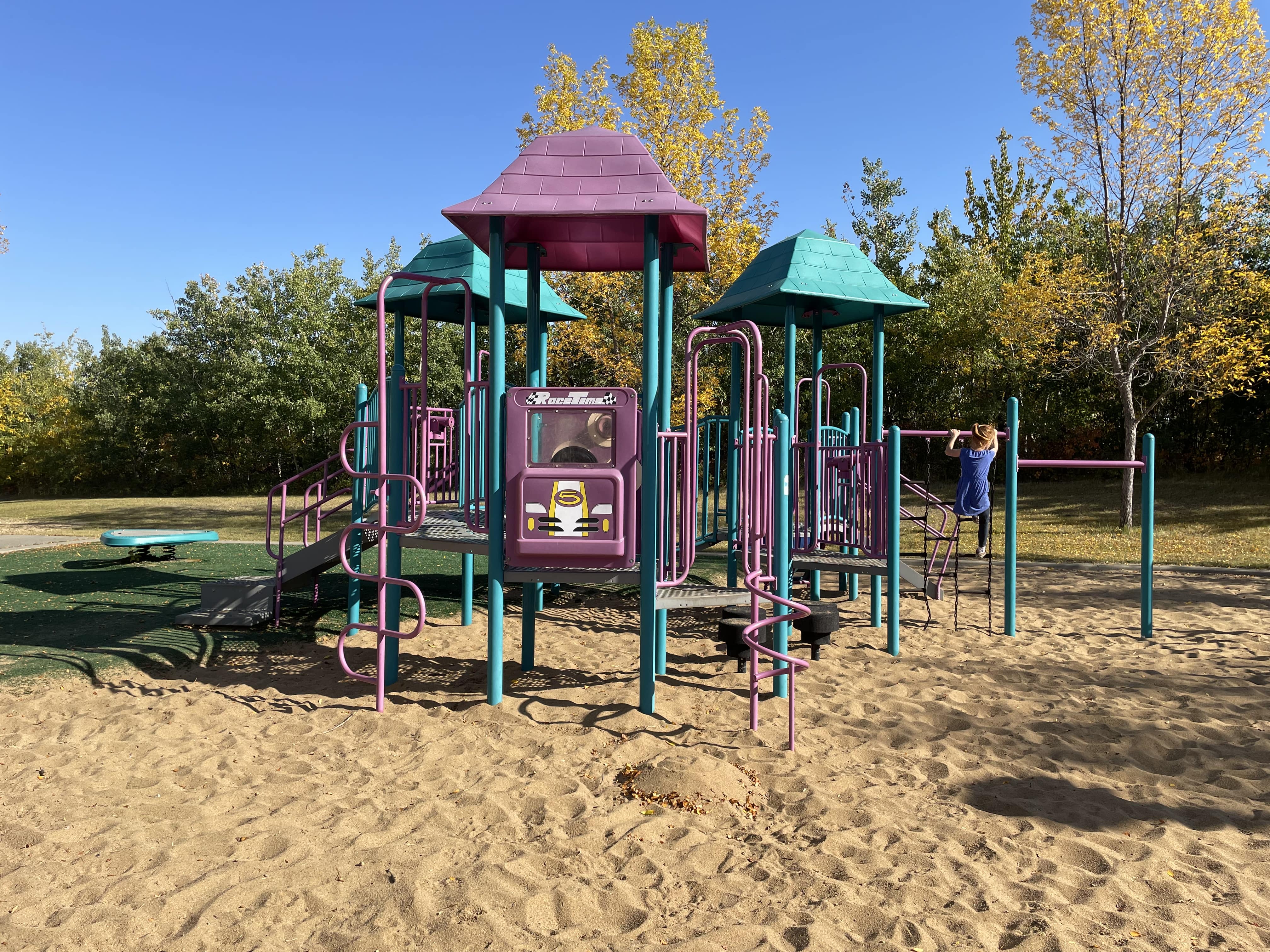 Falconer Heights Playground playground in Edmonton, AB with artificial turf base, teal and lavender colors, supernova circle
