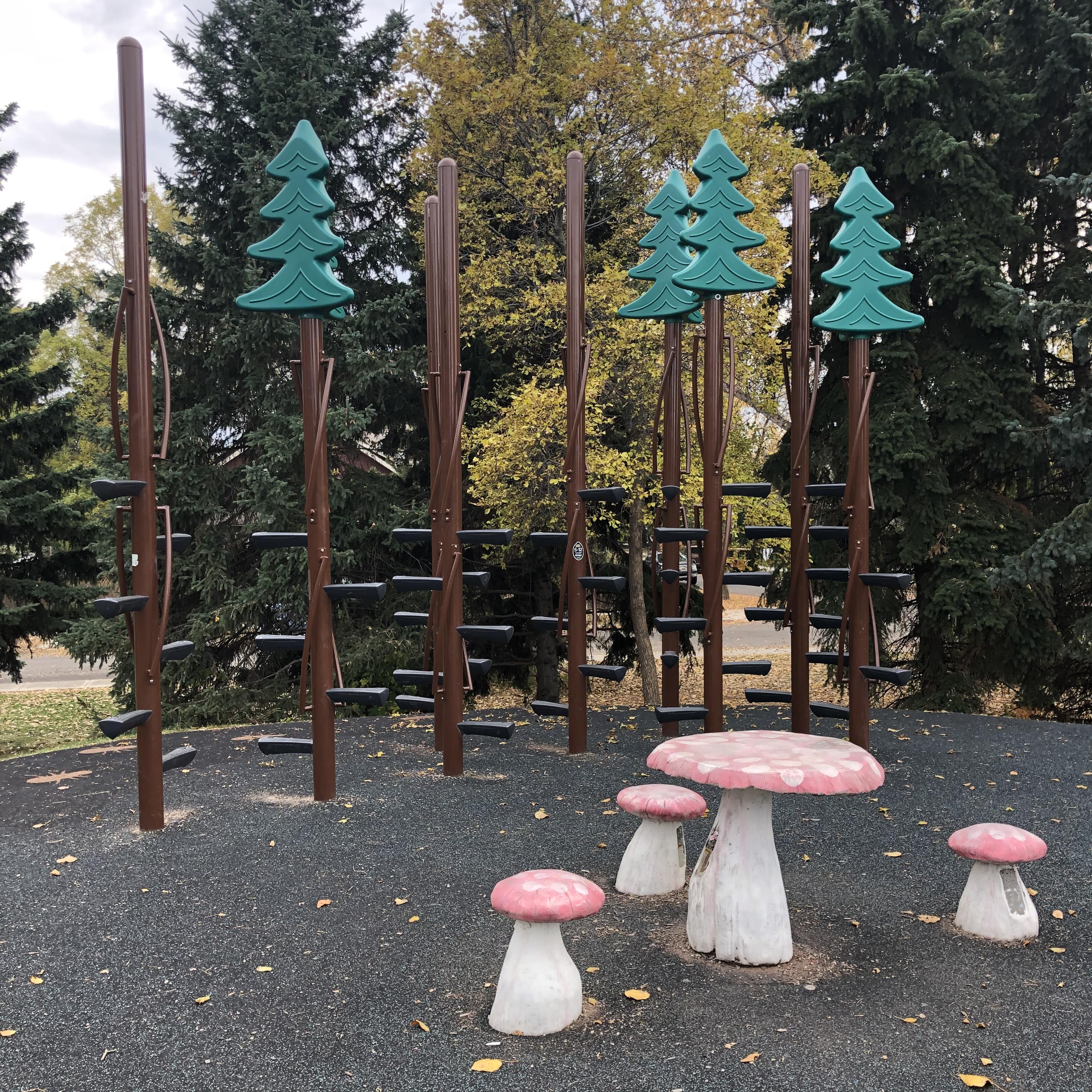 Tall brown poles with staggered black stepping platforms topped by green stylized tree shapes; pink toadstool table set in front.