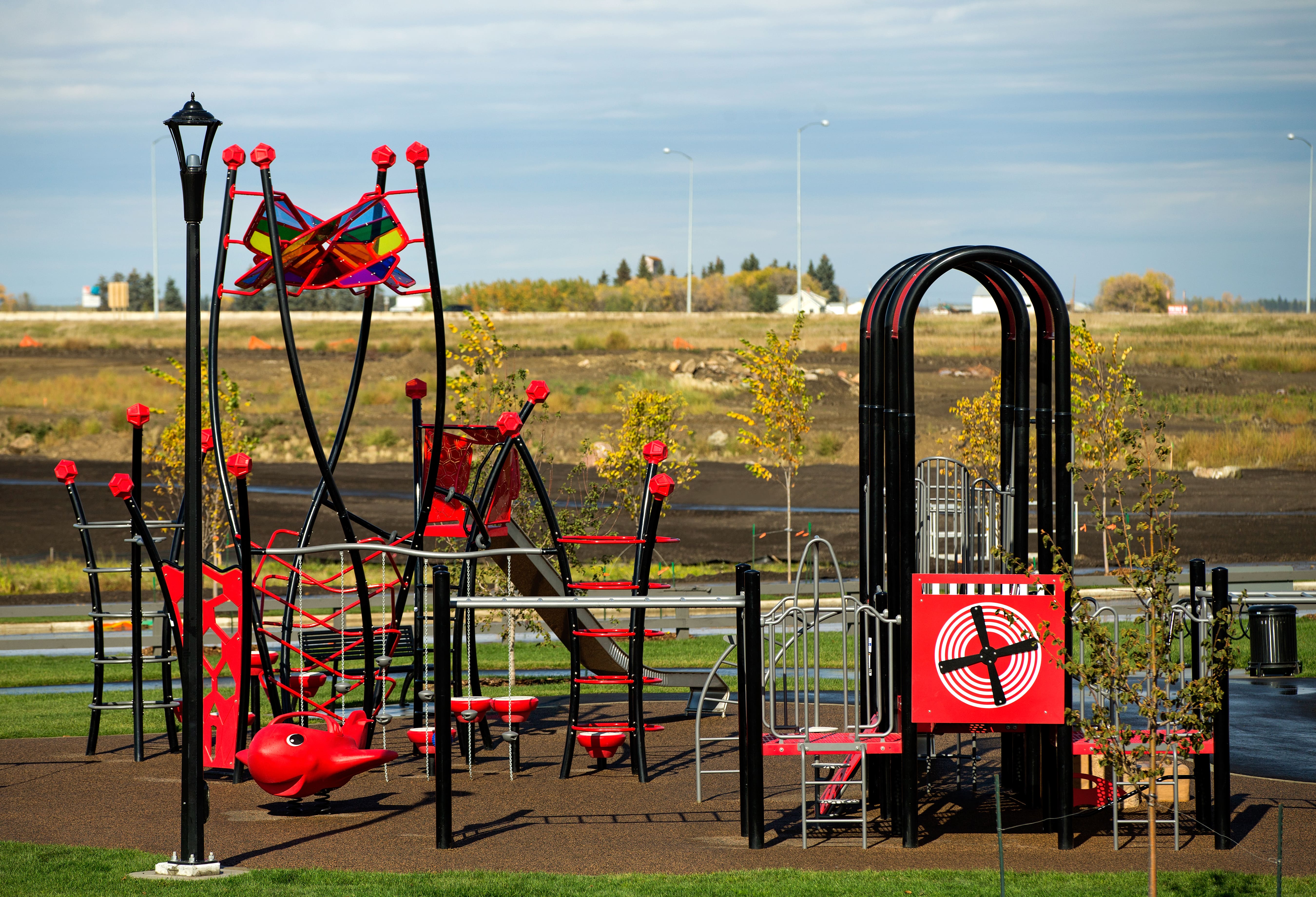 Close view of tall black play poles topped with multicolored translucent airplane-shaped panels and nearby arched red canopies.