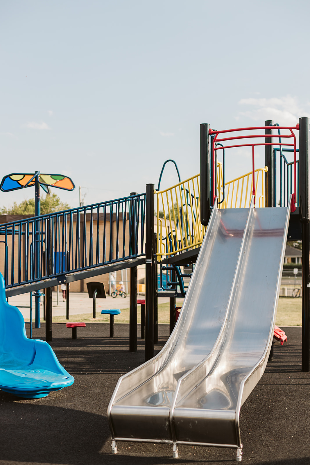 Shiny twin slides descending from a multilevel play platform with a blue ramp, yellow railings and a blue molded seat.