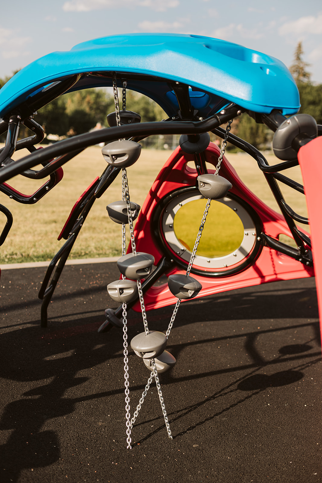 Close view of chain-linked grey stepping holds suspended beneath a blue canopy, with a red play panel and yellow circular window behind.