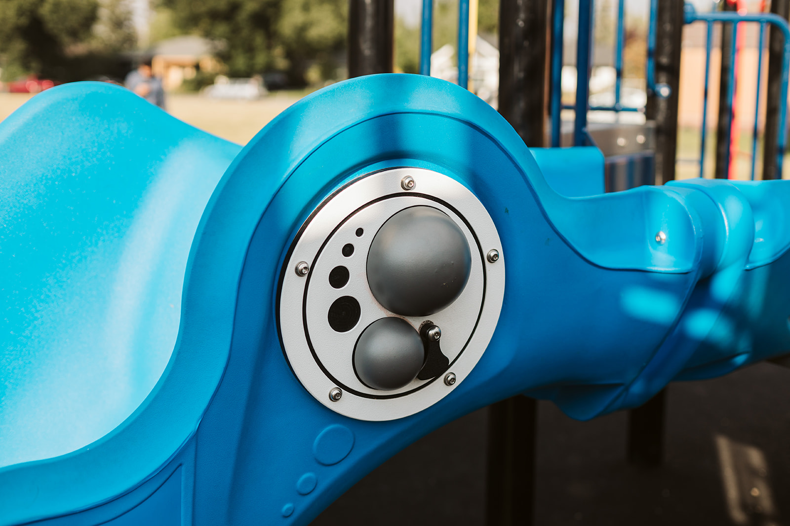 Close-up of a blue molded play panel featuring a circular white disk with grey domed interactive knobs and visible screws.