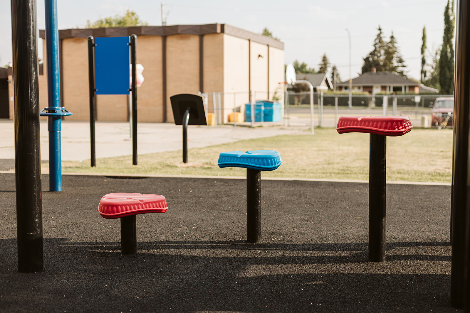 Three low mounted play seats — two red and one blue — on black posts arranged across a rubber playground surface.