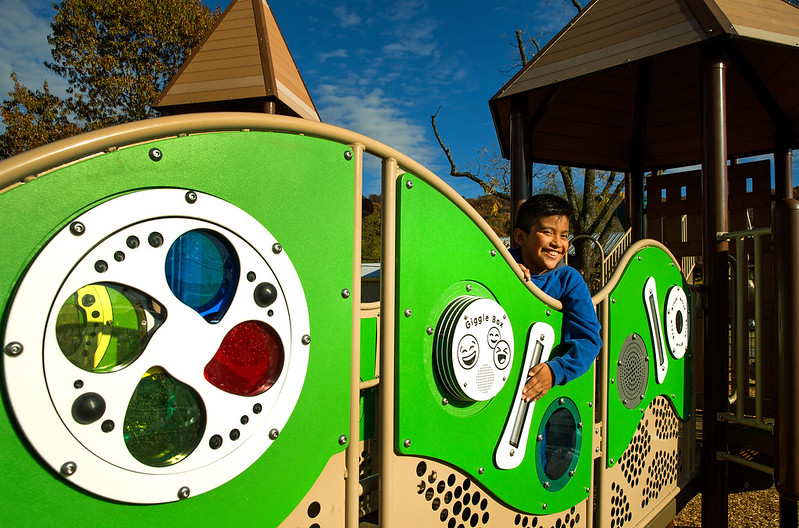 Smiling boy peeks through green playground panels with interactive circles labeled 'Giggle Box'