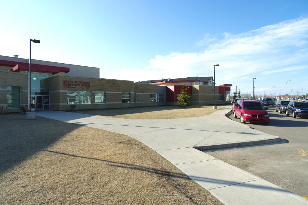 Mattie McClung Elementary School entrance with sidewalk, brown lawn and cars along the curb