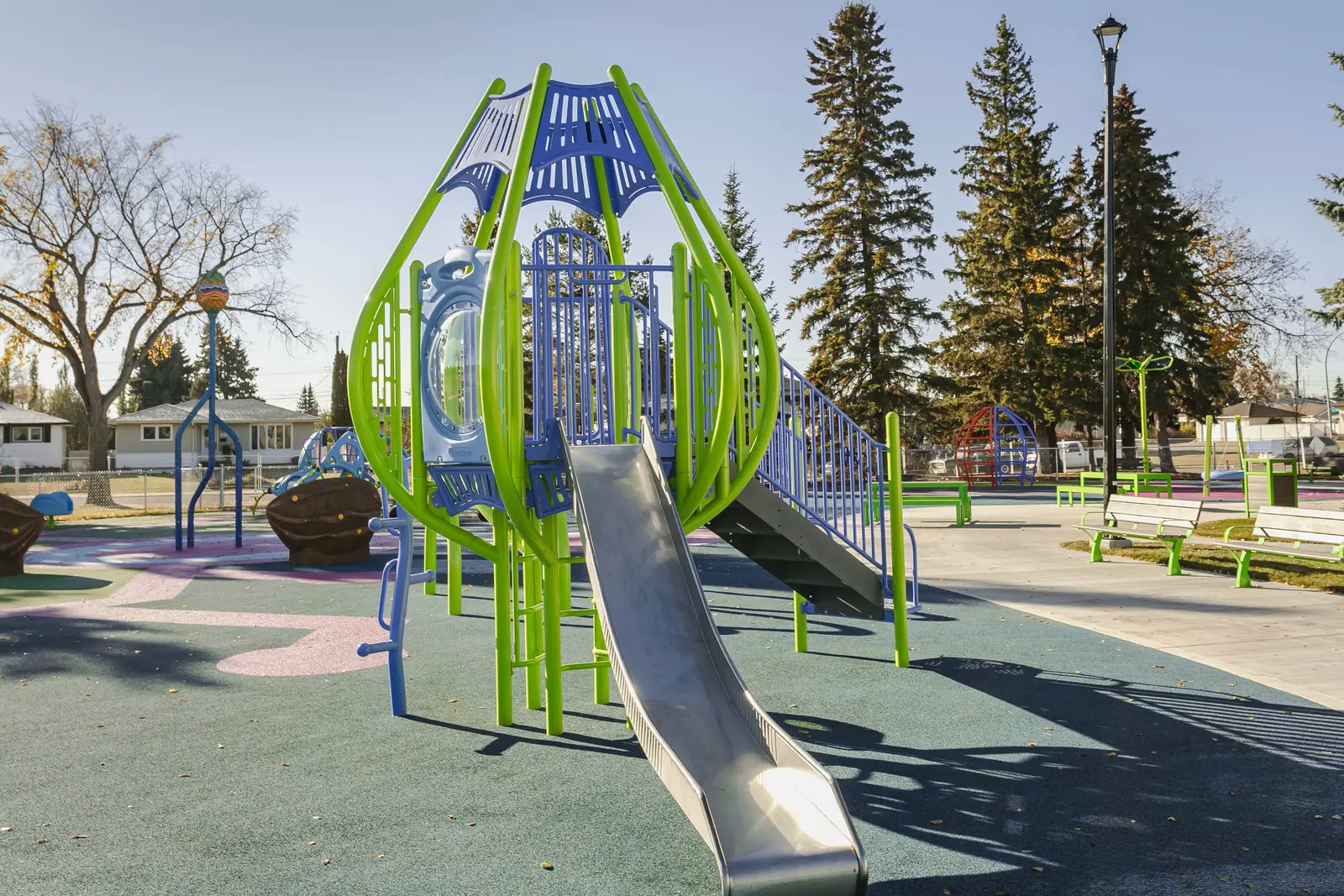 Lime-green tower with a blue roof, porthole panel and stainless steel slide, benches along the path