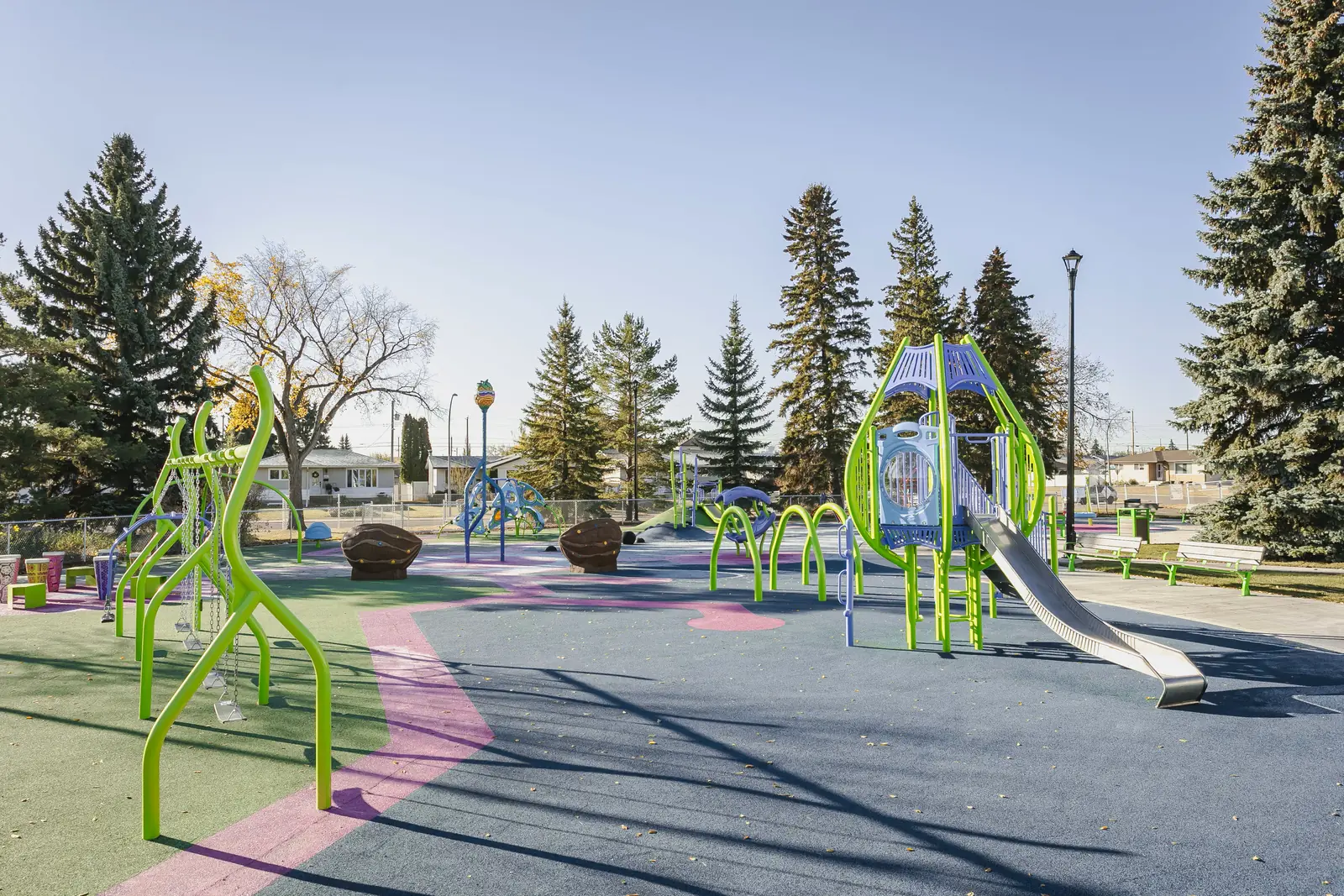Tower and slide, arched hoops, swing frame and seed-pod seats across blue, green and pink rubber