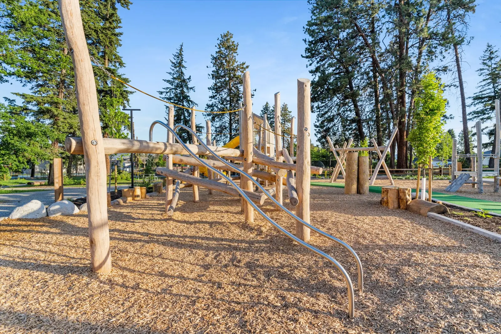 Curved steel climbing bars leading up into a log climbing frame on engineered wood fibre