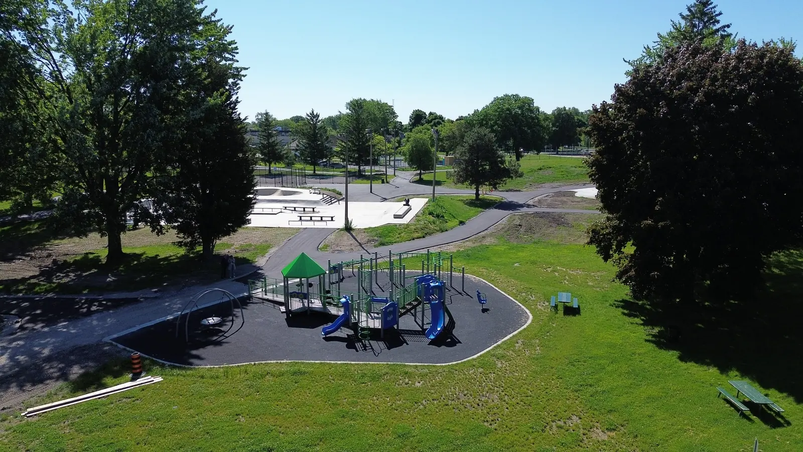 Wide aerial of the play area set in open lawn, framed by mature trees and picnic tables