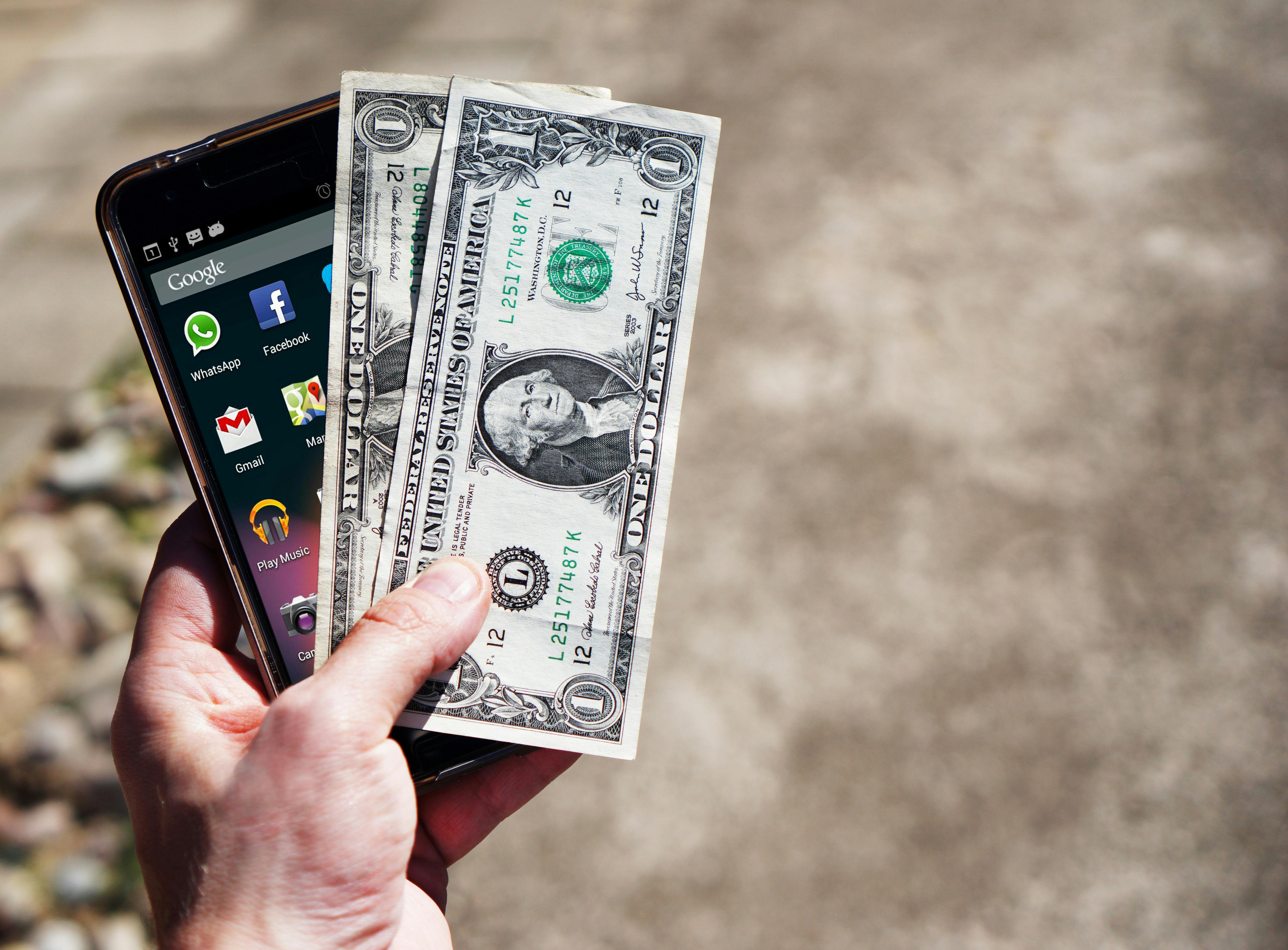 Hand holding a phone and two one-dollar bills