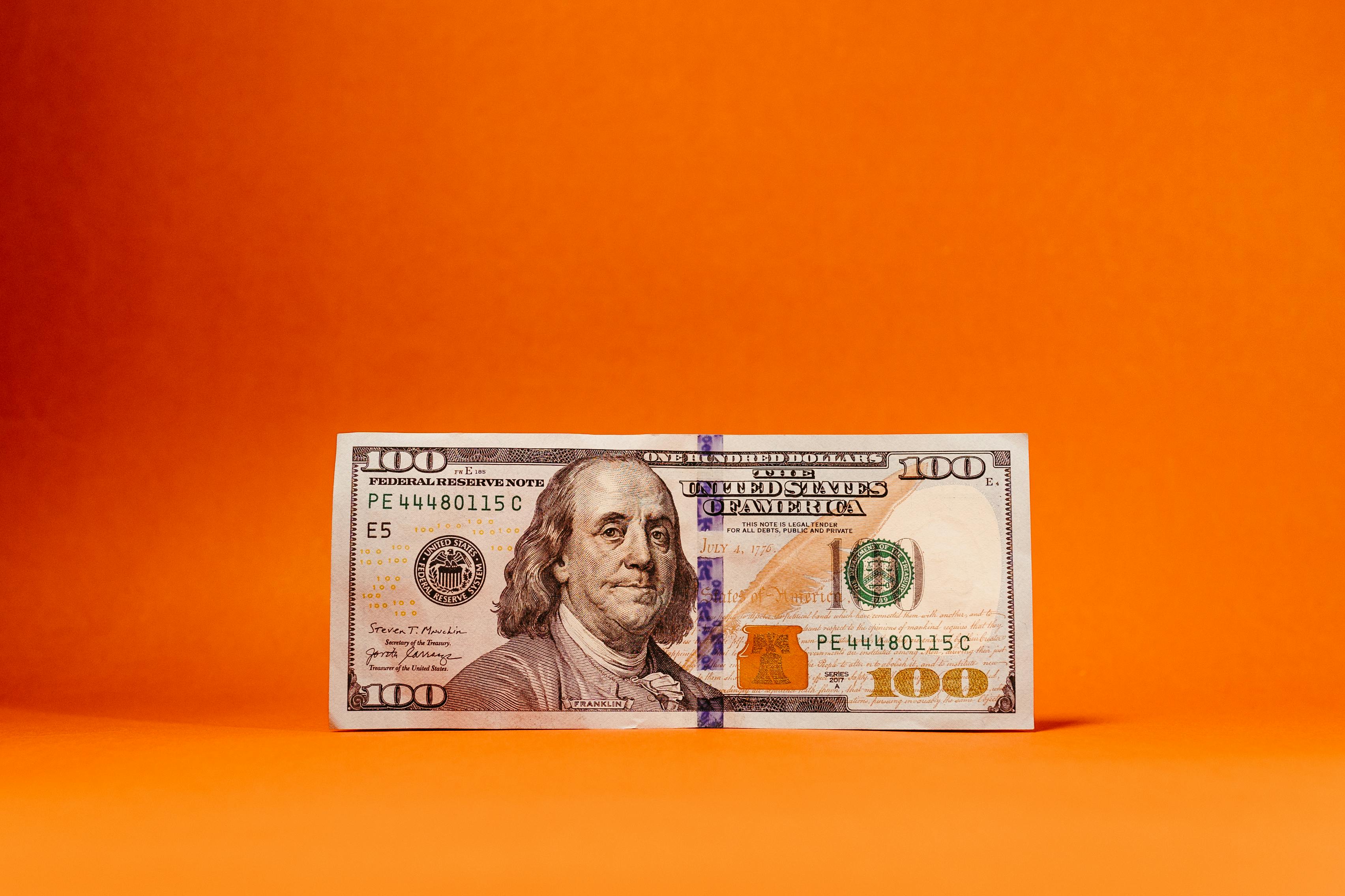 U.S. one hundred dollar bill centered against an orange background.