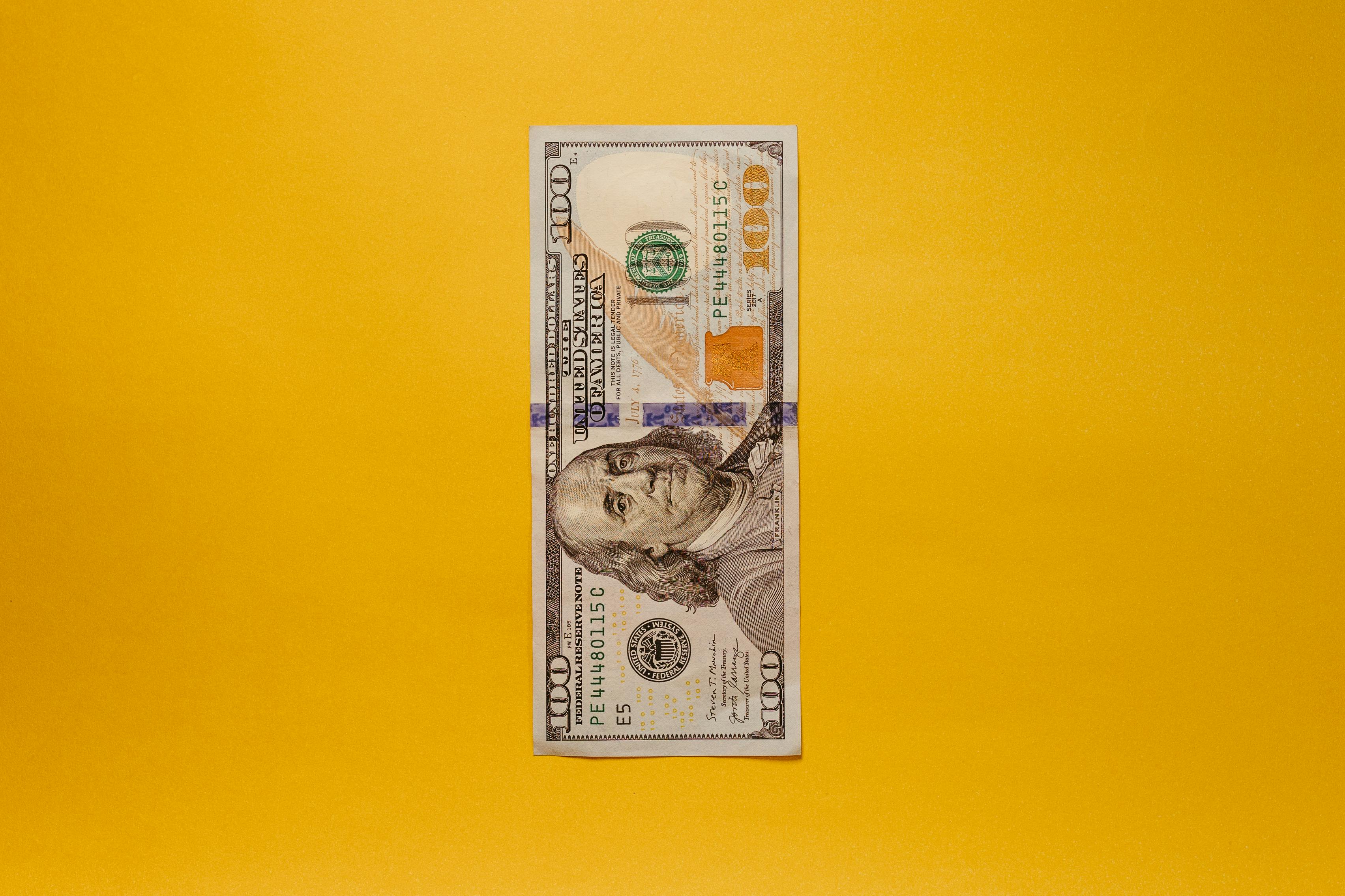 U.S. one hundred dollar bill placed vertically on a yellow background.