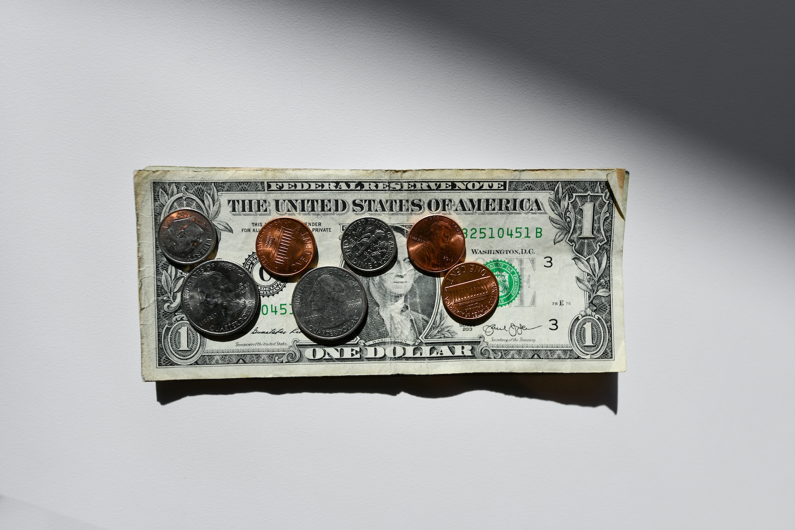 A worn one-dollar bill with several coins resting on top of it against a white background.