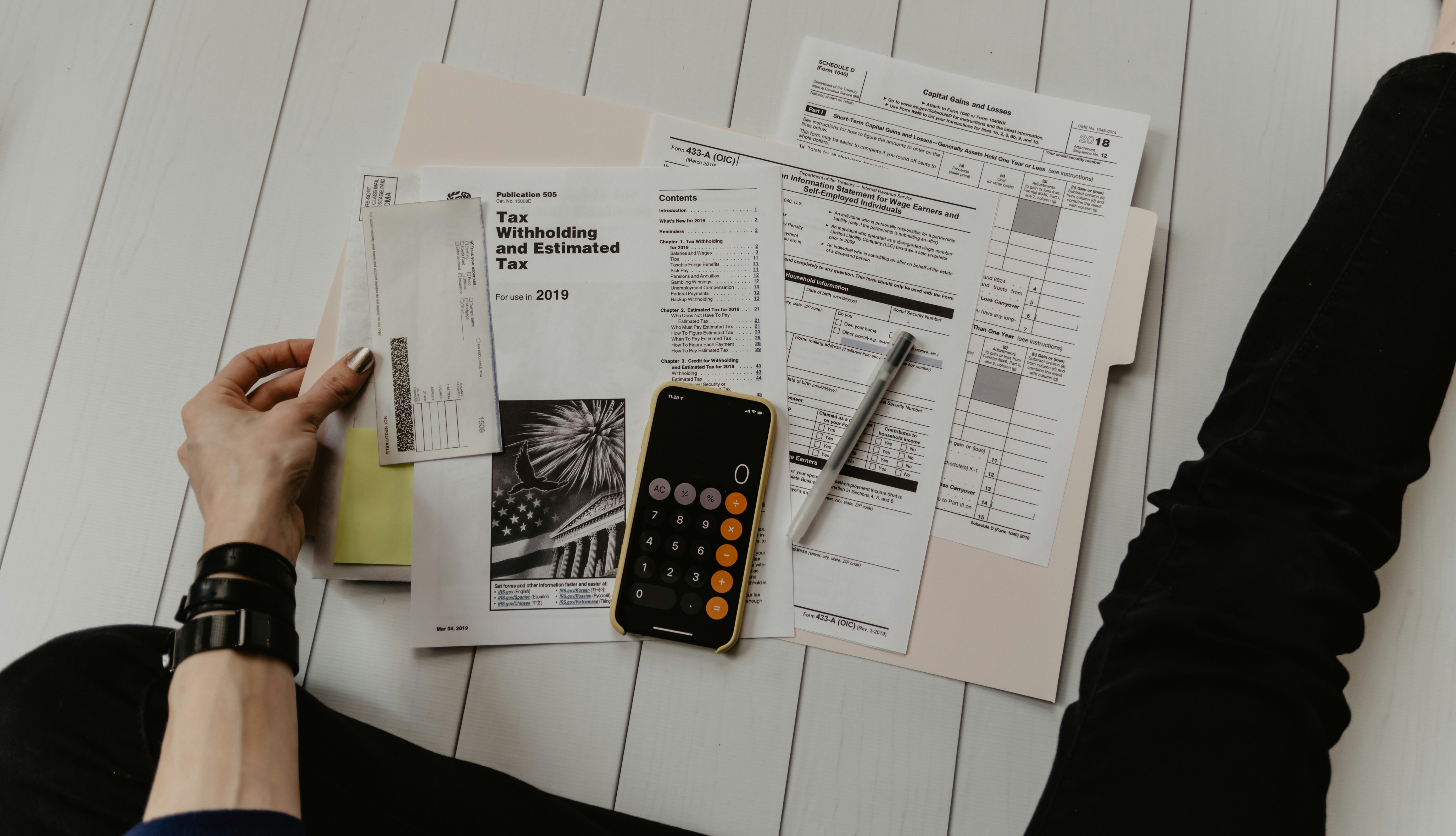 A person holds a check next to tax forms, a calculator app, and a pen spread out on a white surface.