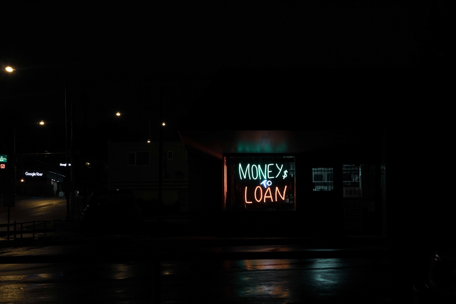A neon "Money to Loan" sign glowing in the window of a darkened storefront at night.