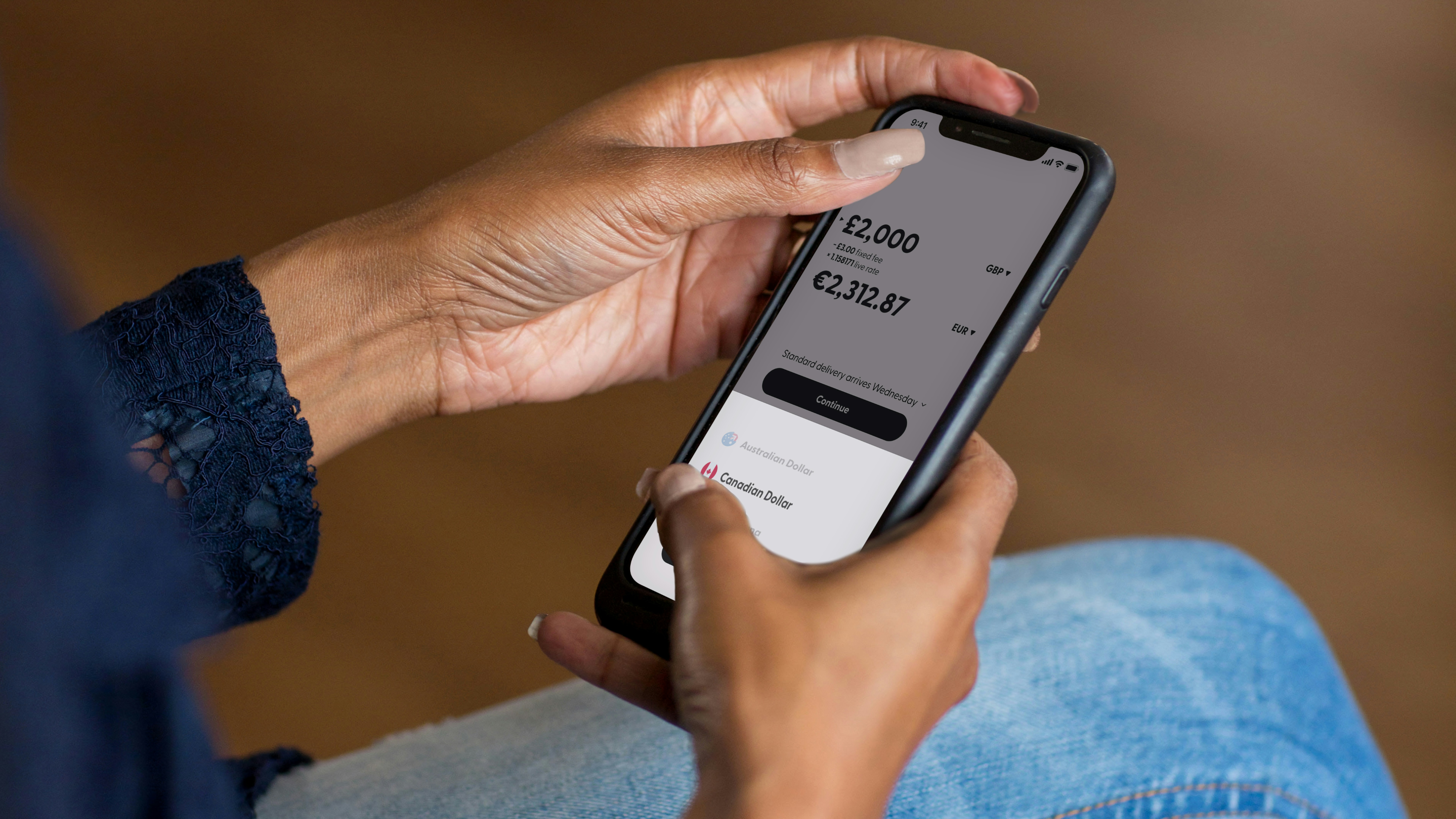 A person holding a smartphone displaying a currency exchange app showing a conversion from British pounds to euros.