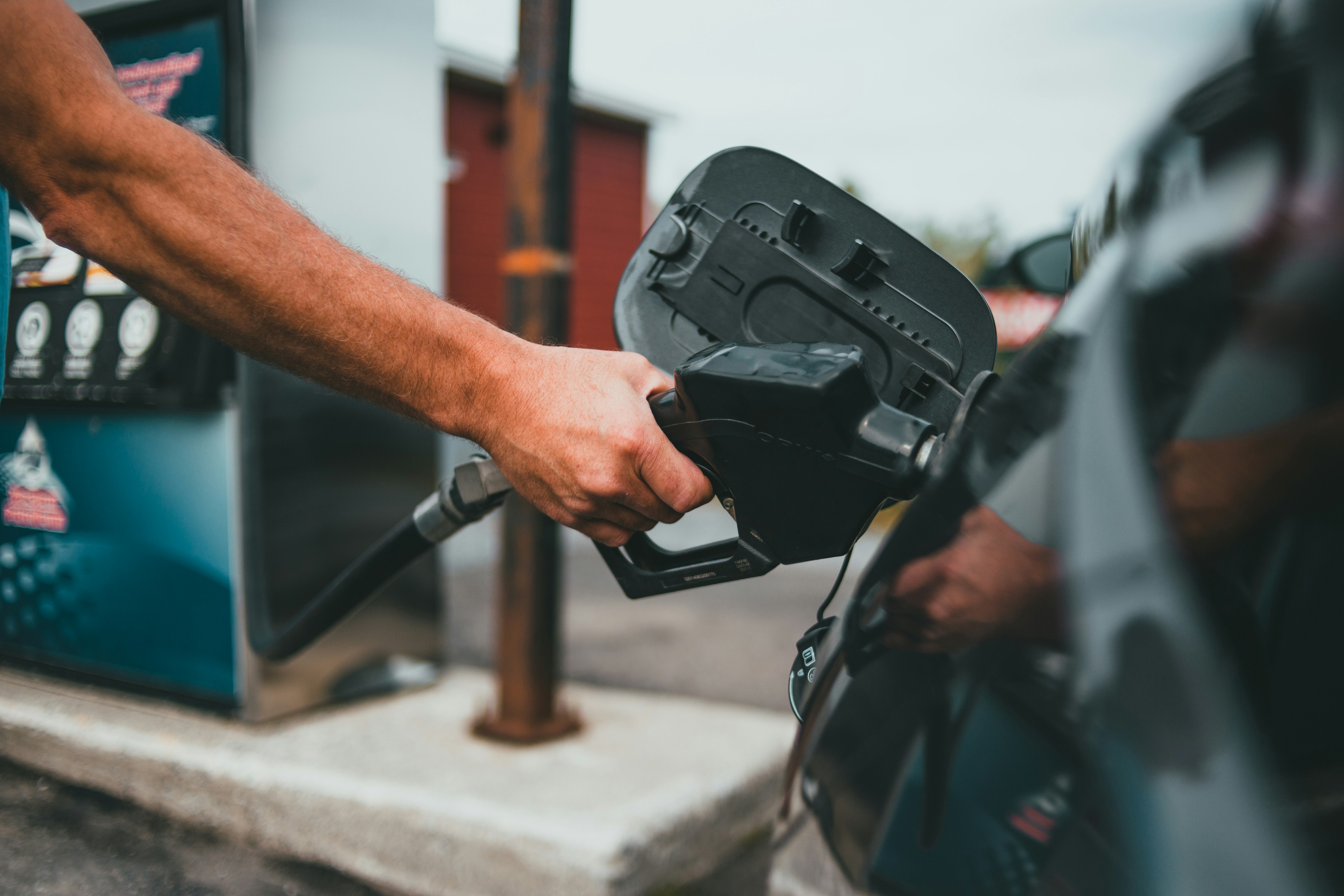 A close-up of a hand inserting a gas pump nozzle into a car's fuel tank at a gas station.