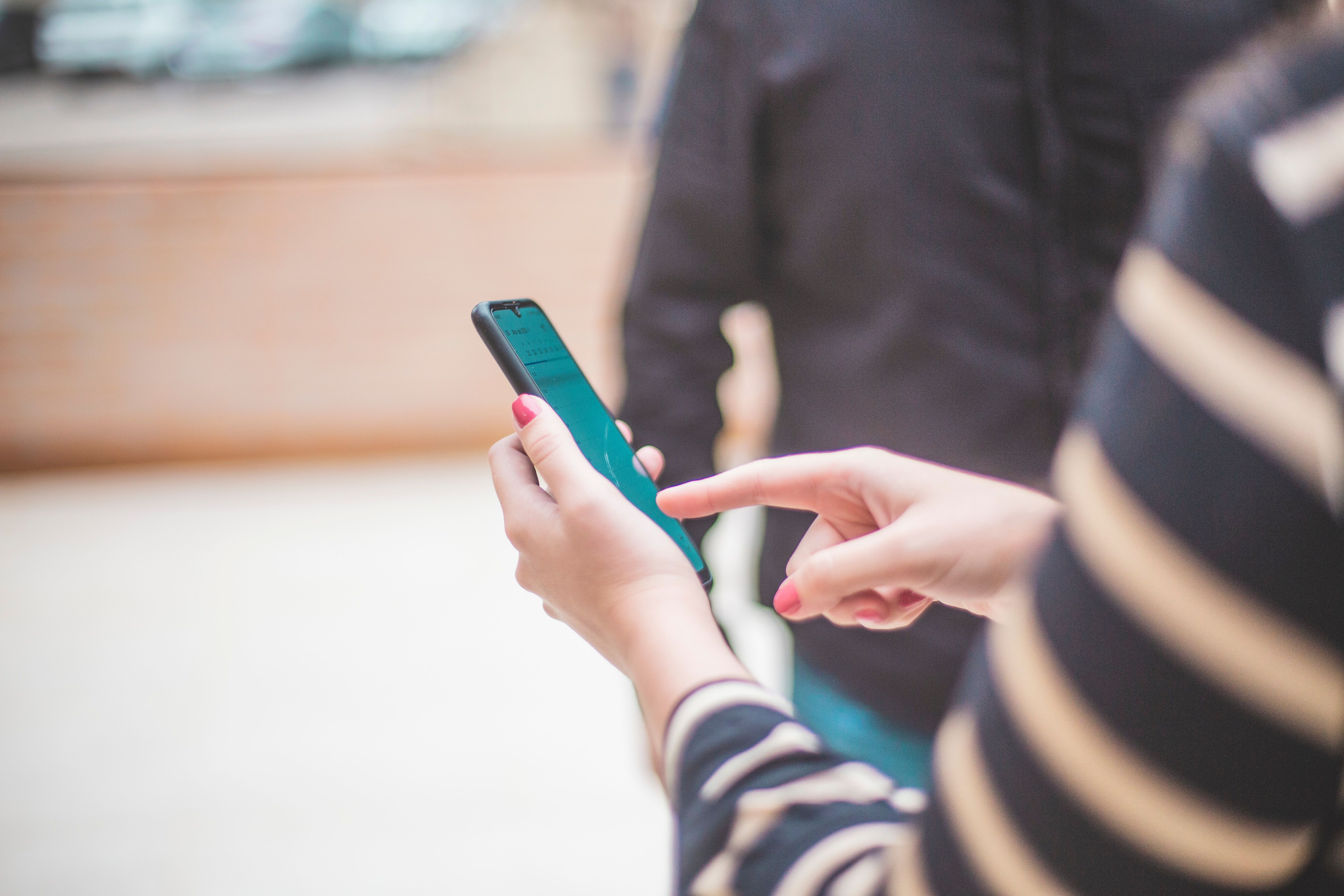 A close-up of hands scrolling on a smartphone with a teal-colored app screen.