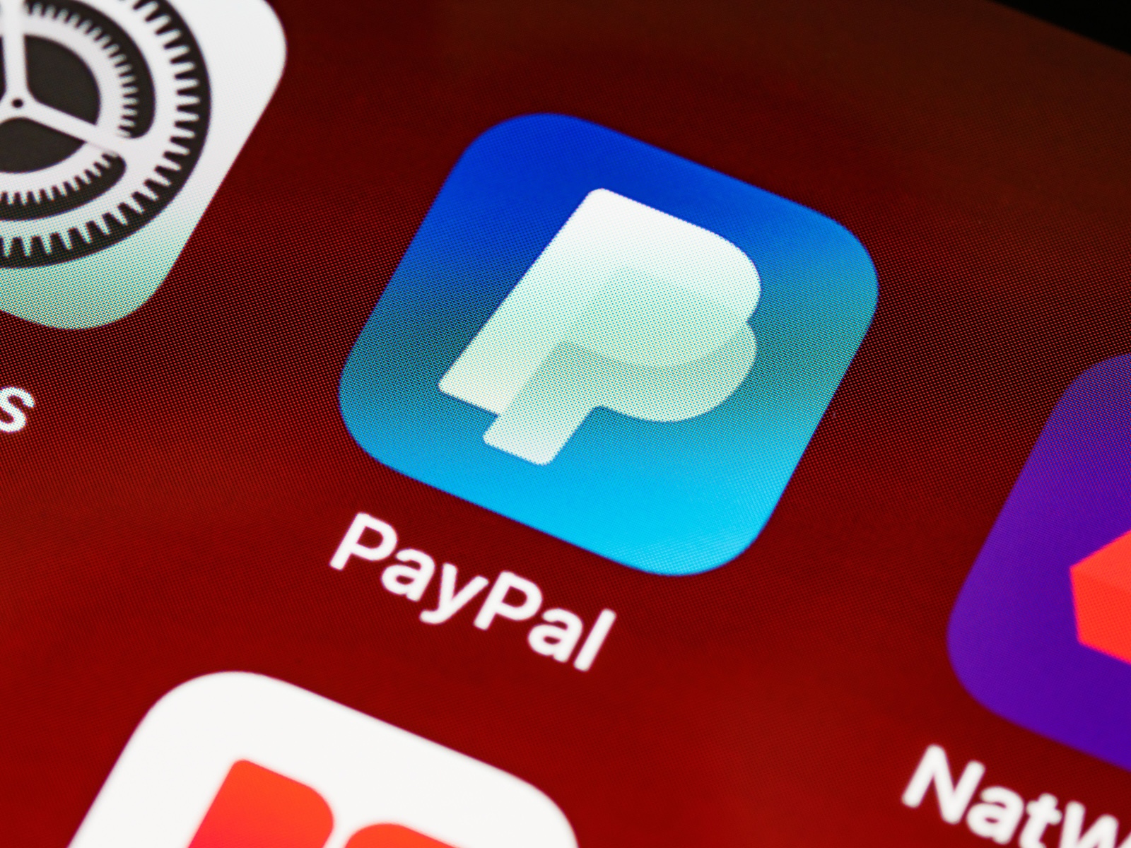 The PayPal app logo on a phone home screen, next to Settings and other app icons.