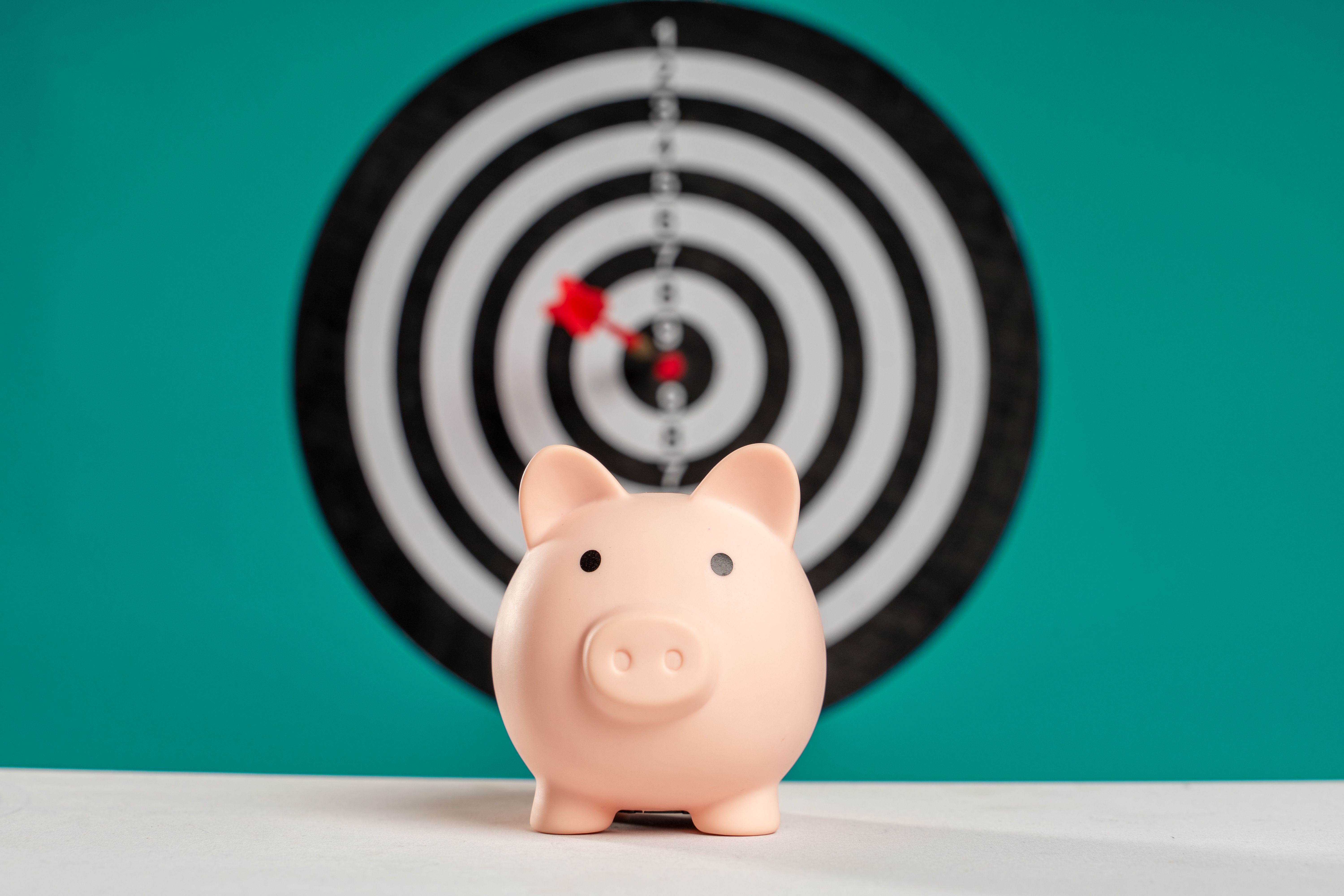 A pink piggy bank sits in front of a dartboard with a dart in the bullseye.