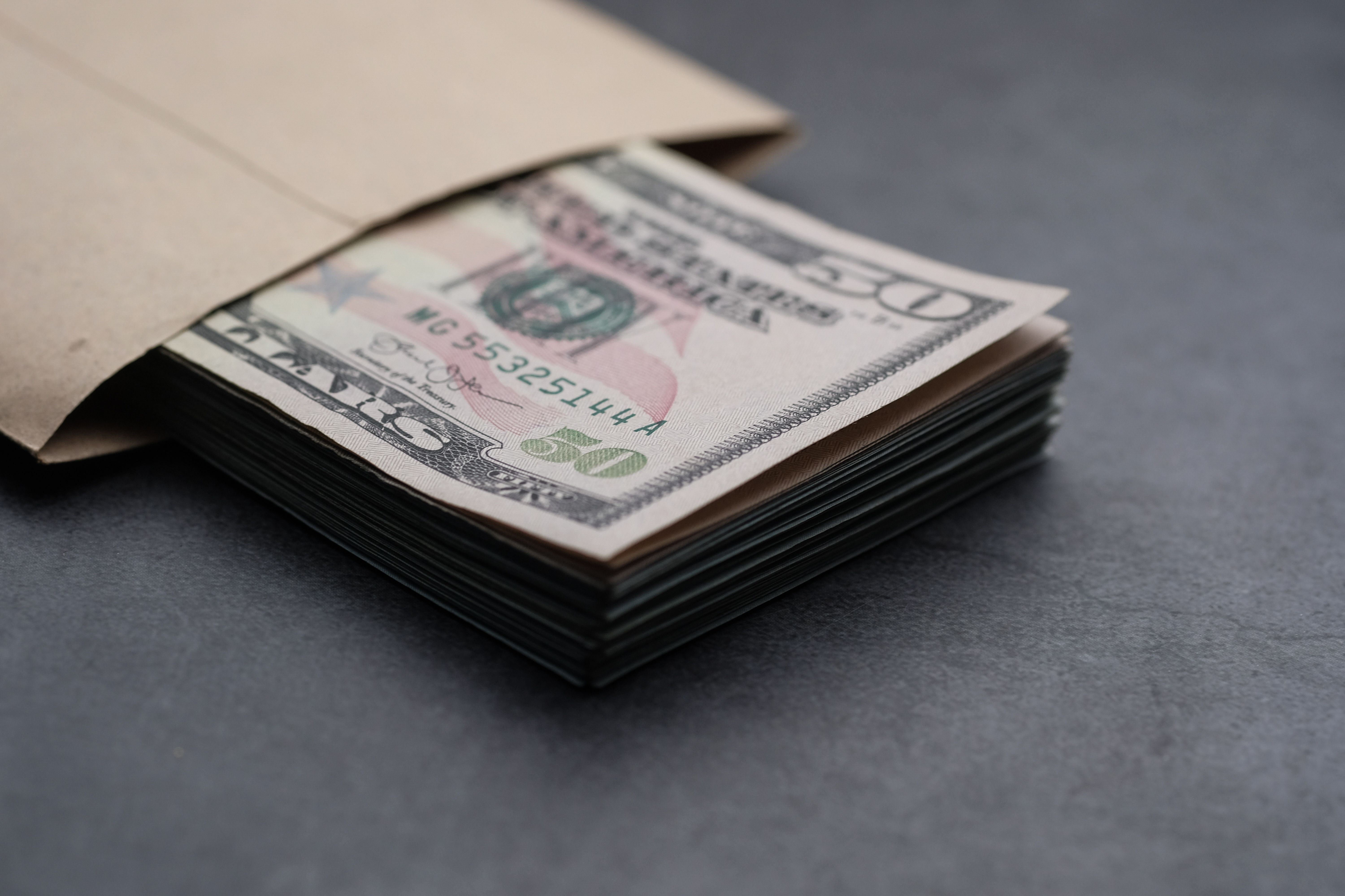 A stack of folded fifty-dollar bills tucked inside a kraft paper envelope.