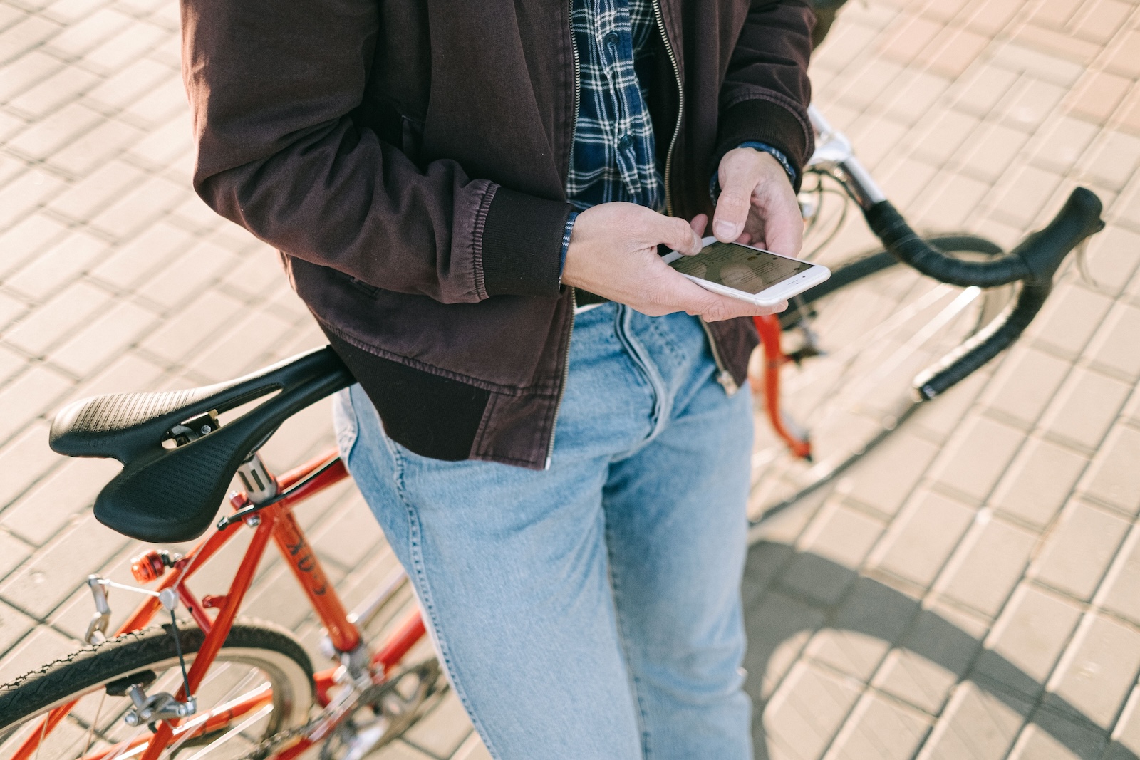 A person standing beside a red bicycle checking their phone on a paved street.