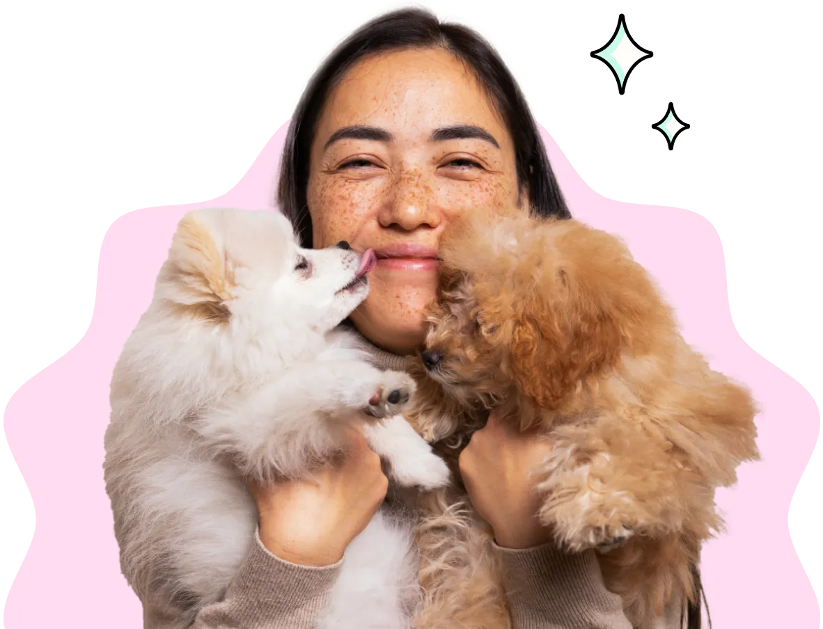 A woman holding up two puppies who are giving her kisses.