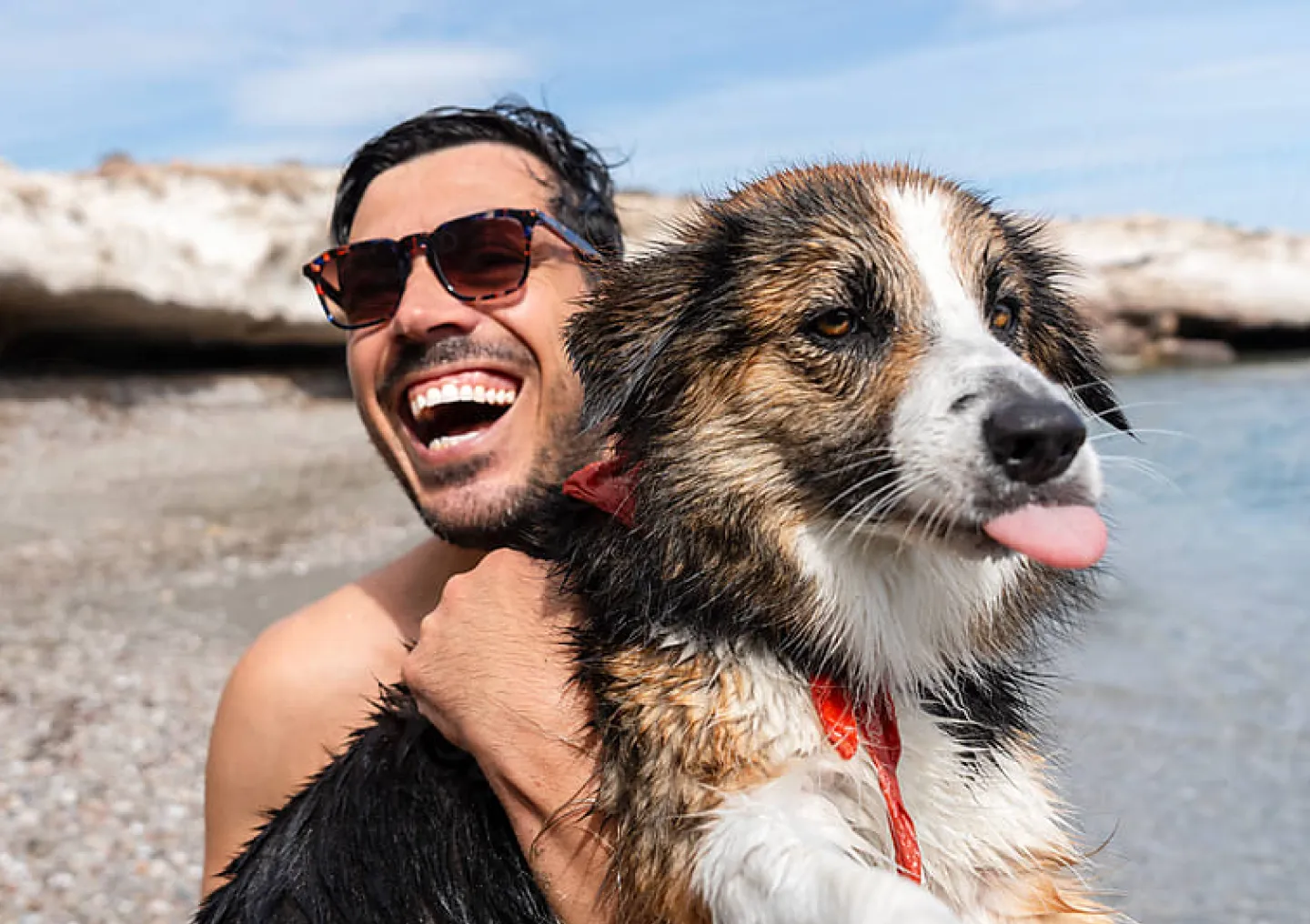 A man holding his wet, displeased dog up at the beach.