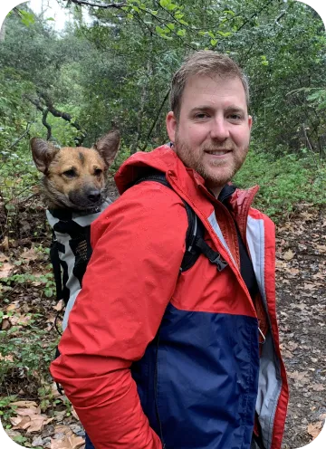 A Fetch employee hiking with their dog in a backpack.
