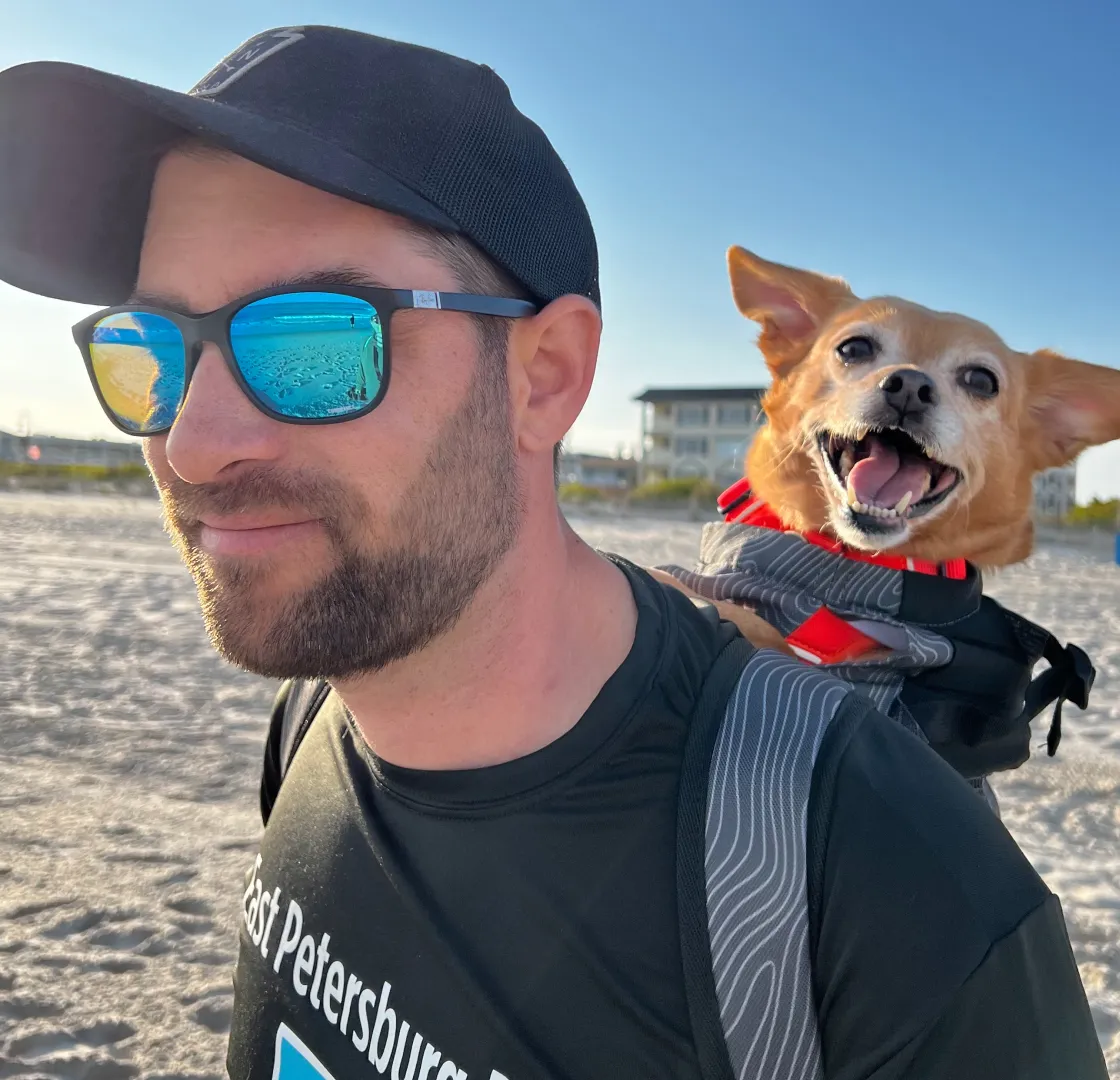Fetch employee Bill T. walking on the beach with his dog in a backpack.